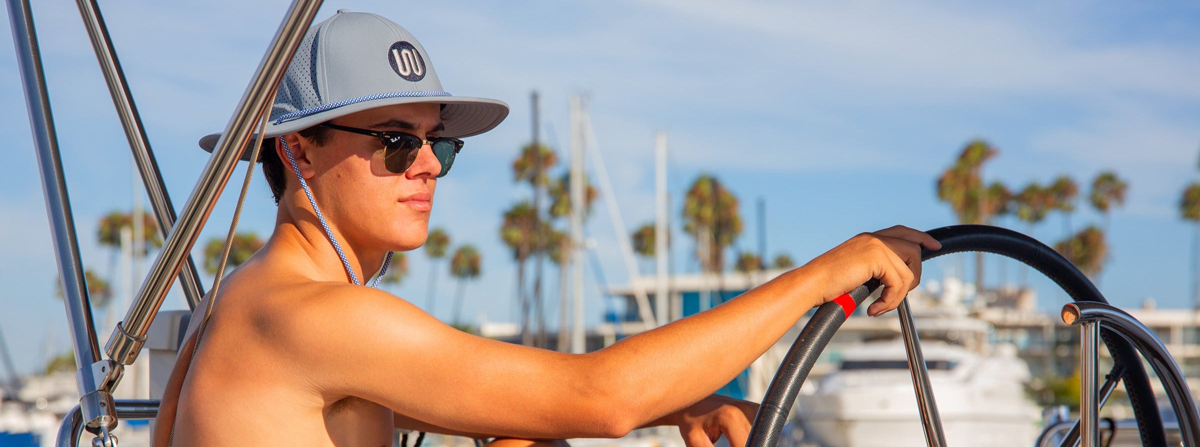Person steering a sailboat with palm trees and water in the background